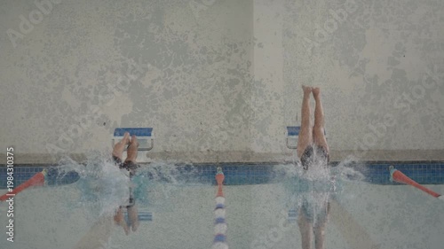 Starting horn sounding, two swimmers simultaneously pushing off, diving into water to begin heat