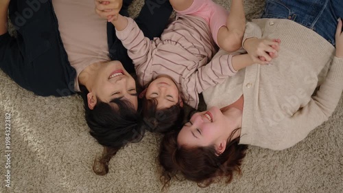 Joyful Asian family with little daughter lying together on carpet at home