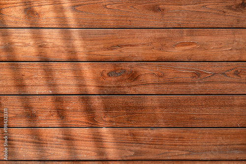 Horizontal brown wood planks background featuring natural grain and dappled sunlight.