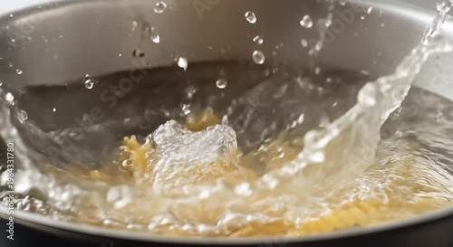 yellow pasta dropping into boiling water in skillet splash closeup