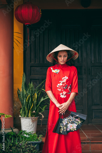 A woman in a traditional Vietnamese costume, a conical hat with a fan in her hands in the ancient district of Hoi An.