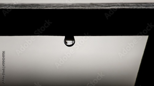 A glistening water drop hangs under a dark eave, reflecting soft light, tranquil and striking against gradient gray.
