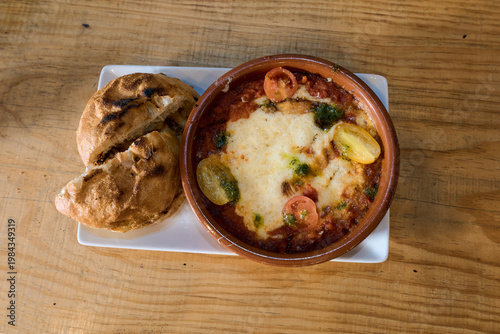 Shakshuka dish on wooden table with grilled bread