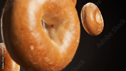 Dynamic advertising of premium bagels cascading in slow motion against a dark studio background, captured from an eye-level viewpoint.