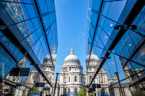 St paul's cathedral's dome reflecting in the glass facade of one new change against a blue sky