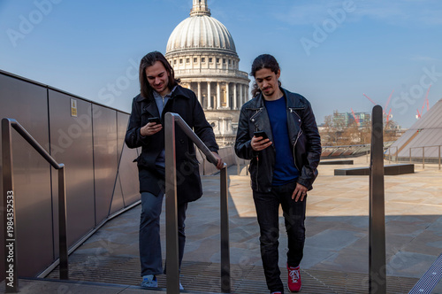 Two young men absorbed in their mobile phones while walking downstairs in london