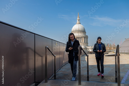 Men walking on a modern rooftop with st paul's cathedral looking at and using smartphones