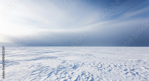A vast snowy landscape under a cloudy blue sky with sunlight shining through