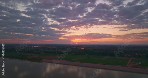 An aerial hyperlapse captures a dramatic sunset over the Mekong River, where golden light spreads across riverside farmlands and rural landscapes. Dramatic Evening Skies Above Mekong Riverside