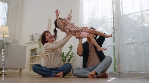 Asian parents lifting and playing with their daughter in living room