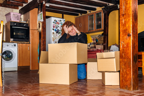 Vászonkép Woman feeling overwhelmed by moving, sitting with hands on head near cardboard b
