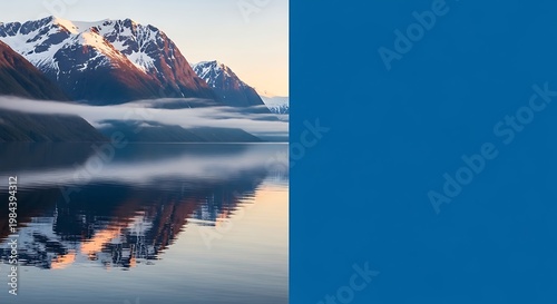 Majestic snow-capped mountains reflected in calm water at sunrise with ethereal mist swirling around the peaks, creating a serene and breathtaking natural landscape.