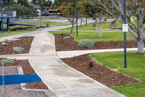 Valokuva Landscaped suburban park featuring a winding concrete footpath with  well-defined mulched garden bed edges, native plantings, manicured green lawn