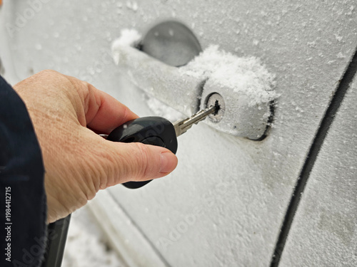Hand trying to open frozen car door lock with key in snowy winter conditions