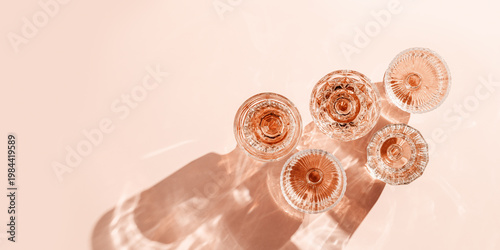 Fotografie Wine Glasses of rose wine on pink background, sun flare and reflection from sunlight