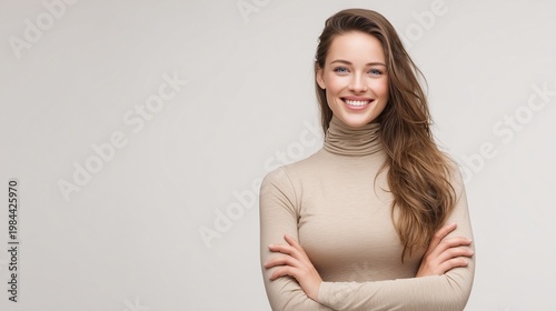 Smiling young woman with brown hair wearing colorful floral mesh top, arms crossed against grey background