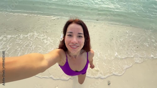 Woman taking selfie while standing in shallow ocean water on tropical Maldives beach. Concept of travel, vacation, summer, tourism, lifestyle, happiness