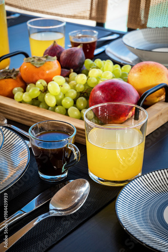 Close-up of a stylish breakfast setup featuring fresh grapes, figs, persimmon, and peach served with coffee and orange juice on a modern table. Clean composition highlighting healthy eating and lifest