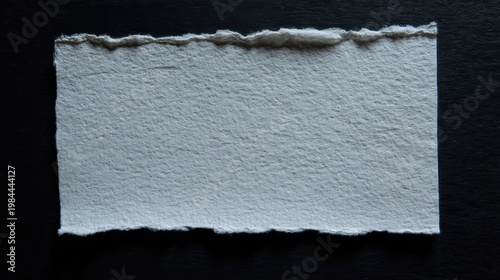 A torn edged light gray handmade paper on dark background with visible texture and natural fibers.