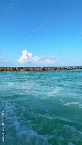 View from moving boat over ocean toward tropical Maldives island with villas and blue sky. Concept of travel, tourism, vacation, seascape, island life, journey. Vertical video