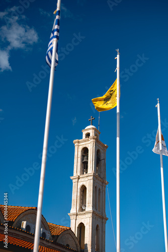 Apostolos Loucas Church bell tower with flags in Kolossi. Limassol District, Cyprus