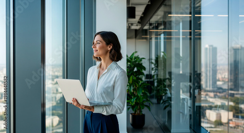 Businesswoman with laptop looking out window at city skyline