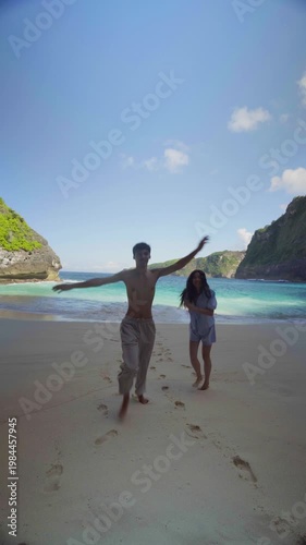 Couple standing on the beach at Kelingking on Nusa Penida, Bali, looking at ocean waves and enjoying romantic tropical scenery