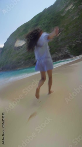 Young woman running on the beach below Kelingking cliffs on Nusa Penida, Bali, enjoying ocean waves and tropical freedom.