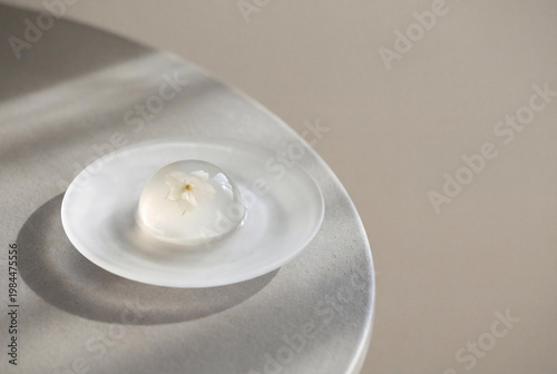 Minimalist Japanese raindrop cake Mizu Shingen Mochi with edible flower on frosted glass plate for luxury dessert and zen aesthetic.