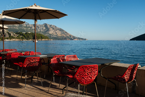 Seaside cafe terrace with red chairs and sea view, outdoor restaurant by ocean, Mediterranean travel lifestyle, summer vacation scene, copy space