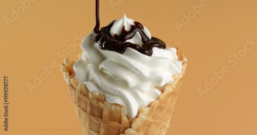 Vanilla ice cream in a waffle cone is being drizzled with chocolate glaze.