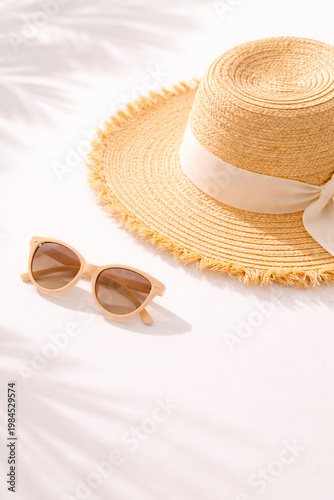 Straw summer hat and sunglasses on clean white background with natural sunlight casting soft shadows, minimalist and elegant composition with copy space.