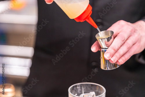 Bartender measuring liquid with jigger in cocktail preparation close up