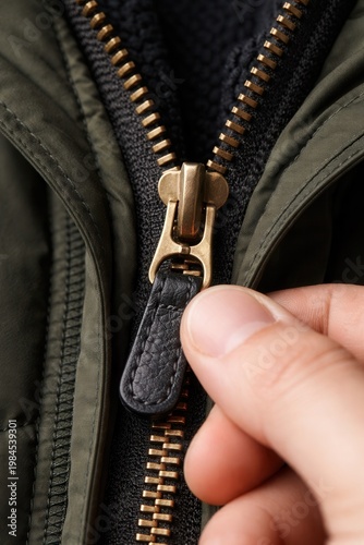 Closeup of zipper being pulled on jacket with hand showing detail of clothing fastener mechanism