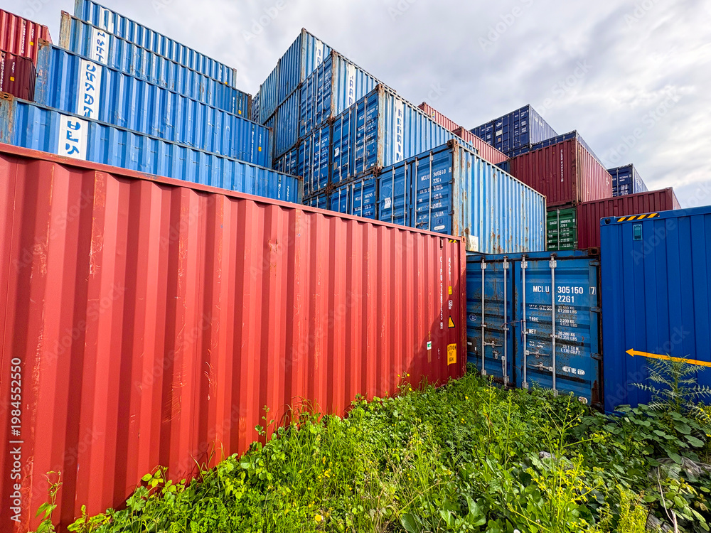 Fototapeta premium Stacked blue and red industrial shipping containers in a freight terminal.