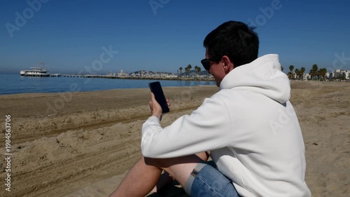 Young man enjoying video call on mobile phone with ocean view.