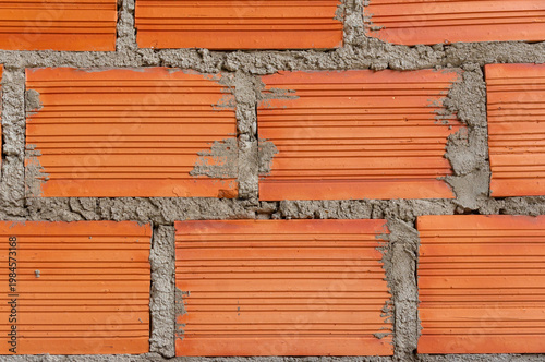 Фотография Orange hollow brick wall - Raw construction: Masonry texture with grooved clay bricks and irregular gray cement mortar