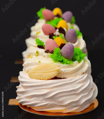 Three Pavlova cakes with meringue, white cream and candies, in line, on black background