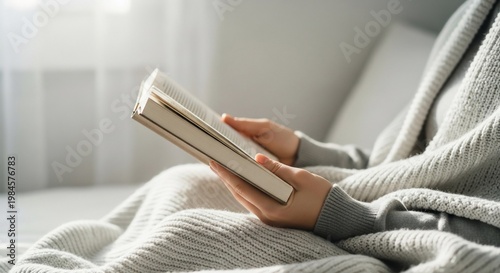Cozy Reading: Woman with Book Under Blanket in Soft Light