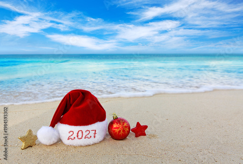 New Year 2027 background with Christmas hat and decorations on Caribbean sand.