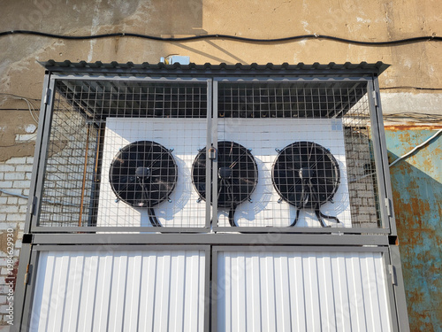 Outside, fans running on the wall in a box behind a grate
