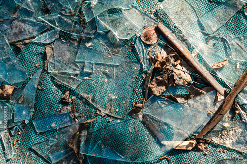 Large pieces of broken glass on ground with dirt and leaves. Crime scene, vandalism, danger concept.