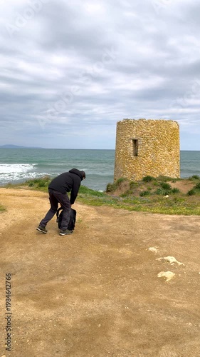 Photographer putting down a backpack on a coastal dirt road with dramatic cloudy sky in natural landscape