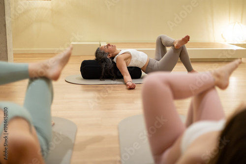 Woman practicing reclined pigeon pose with bolster