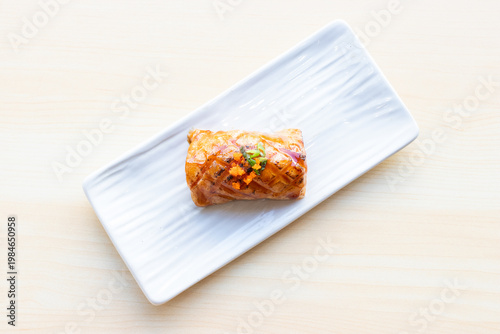 Grilled salmon aburi sushi topped with sweet sauce and tobiko, served on a white ceramic plate over a light wooden table background.