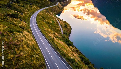 winding asphalt road along calm lake reflecting golden sunset sky, mountain landscape travel path, scenic route, transportation infrastructure, nature exploration