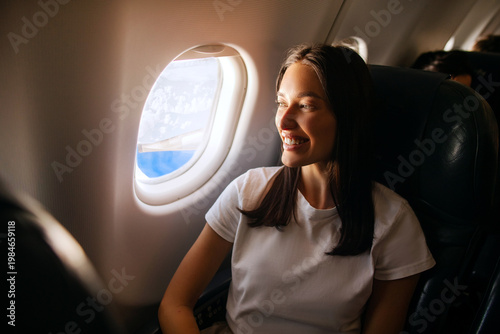 Fotografía Happy lady enjoying the view from her seat in plane while looking at window and