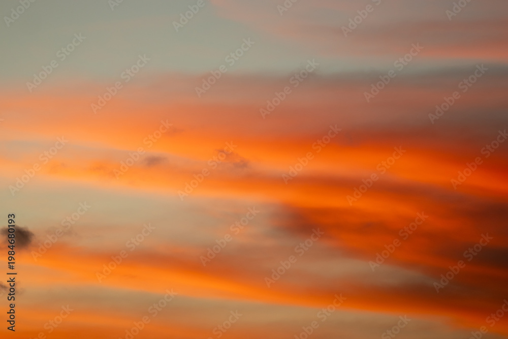 Fototapeta premium Vibrant orange sunset sky with dramatic cloud formations and a smooth gradient background.