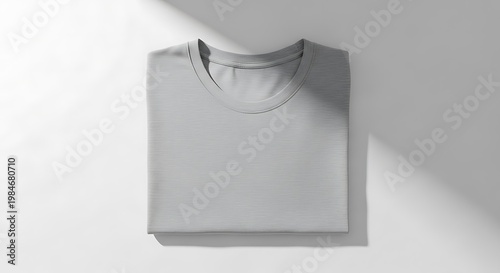 Folded plain grey t-shirt on a white surface with soft light and shadow