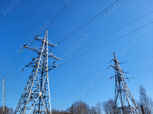 Two tall power transmission poles with wires in a cloudless spring sky